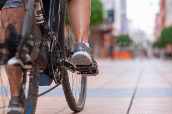 Close up on casual woman\'s legs while running her electro bicycle in urban street
