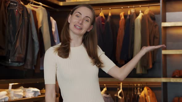 The Saleswoman Smiles and Shows the Clothes in the Costume Shop and Speaks to the Camera alt