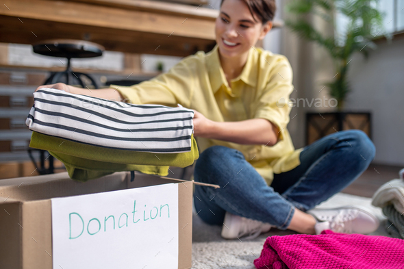 Joyful girl seated on the carpet packing things for donation