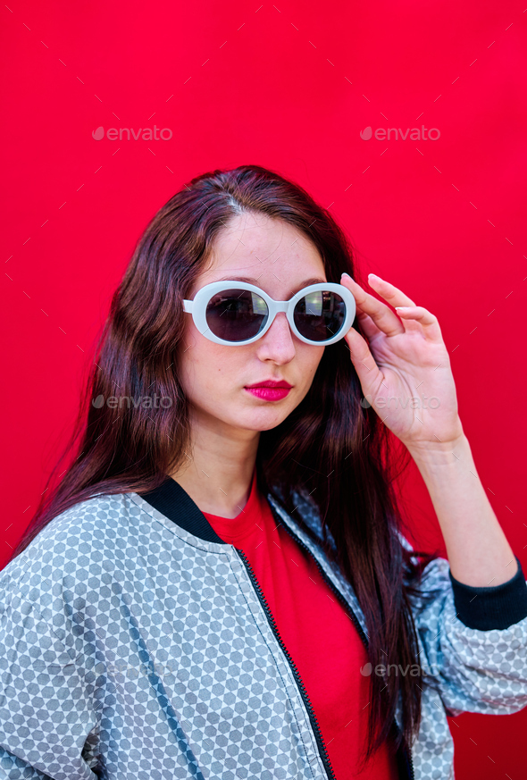 Portrait of a young brunette girl taking off her sunglasses on red ...