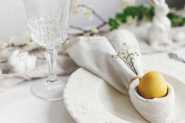 Stylish elegant Easter brunch table setting. Easter egg in bunny napkin, plate, flowers
