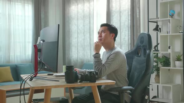 Asian Cameraman Thinking While Using Desktop Computer For Working At Home alt