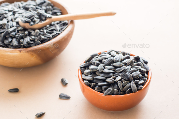 Raw unpeeled sunflower seeds in two bowls on a beige background. Natural source of vitamins and fat