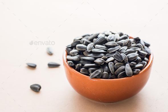 Raw unpeeled sunflower seeds in a bowl on a beige background. Natural source of vitamins
