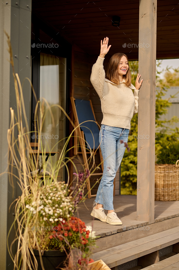 Woman standing on porch of house in greeting