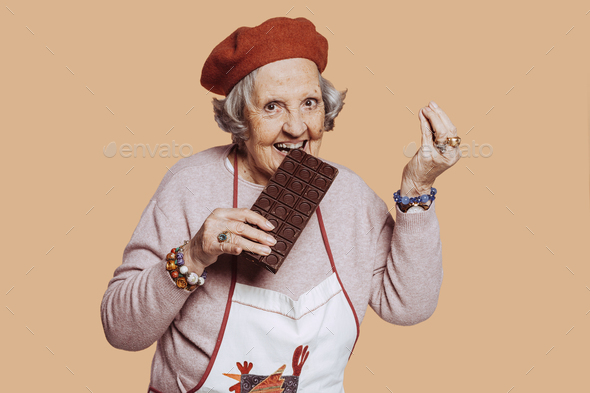 Cheerful elderly grandmother biting into a chocolate bar