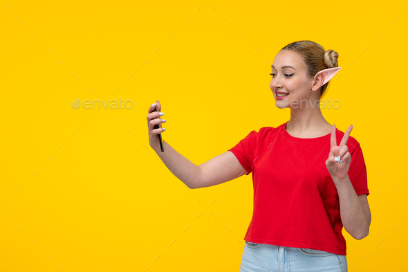 caucasian female in red t-shirt with elf ears taking selfie yellow background girl cartoon