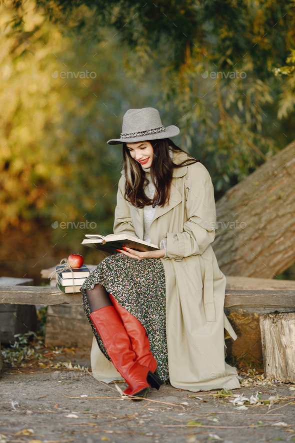 Young woman in a coat sitting on a wooden bench and reading a book - Stock Photo - Images
