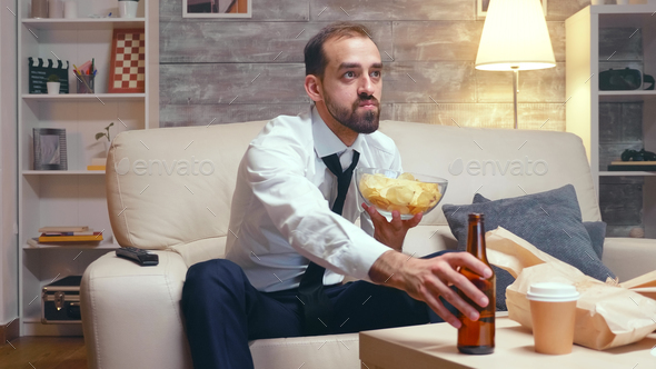 Businessman in formal ear sitting on couch eating chips