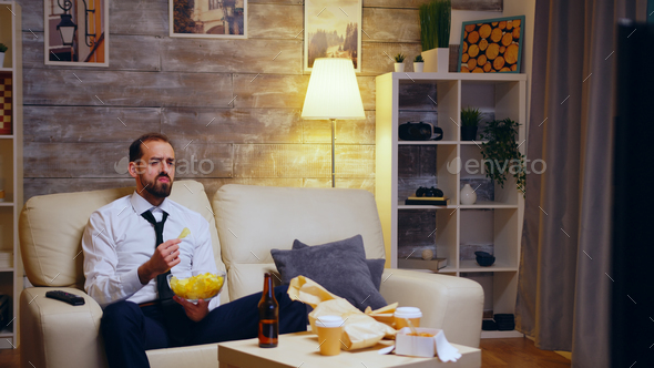Businessman sitting on couch eating chips