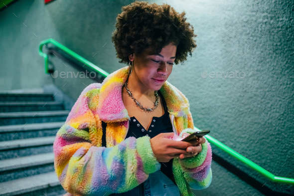 Young black woman indoor underground station using smartphone surfing web