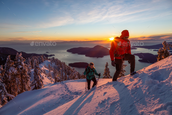 Adventure seeking man and woman are hiking to the top of a mountain during winter sunset