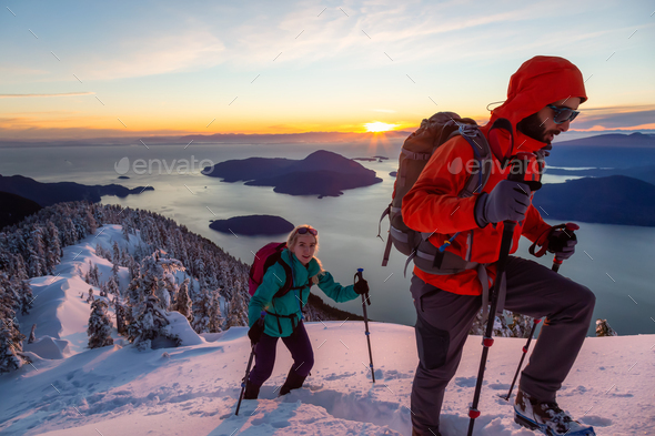 Adventure seeking man and woman are hiking to the top of a mountain during winter sunset
