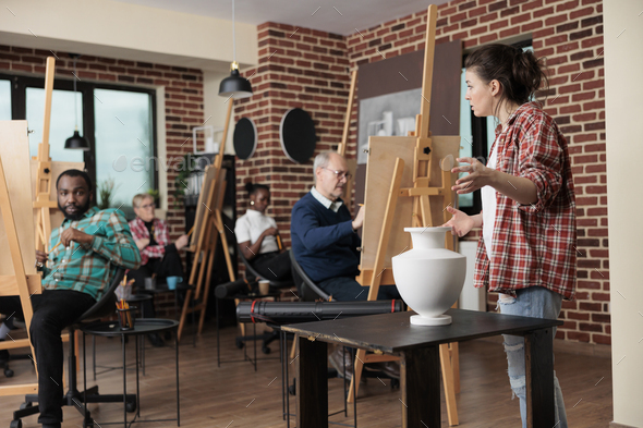 Painter teacher supervising senior man while drawing vase model on canvas