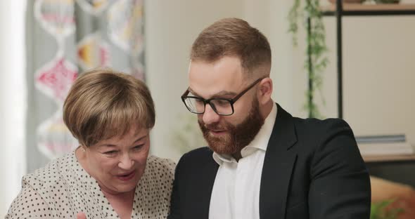 Smiling Retired Mature Woman and Handsome Young Man in Glasses Possing for Selfie at Home alt