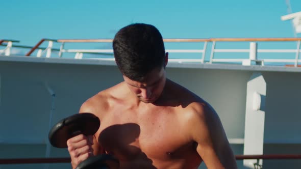 Athletic Handsome Man with Naked Torso Practice Biceps Exercise with Dumbbell Onboard Cruise Ship