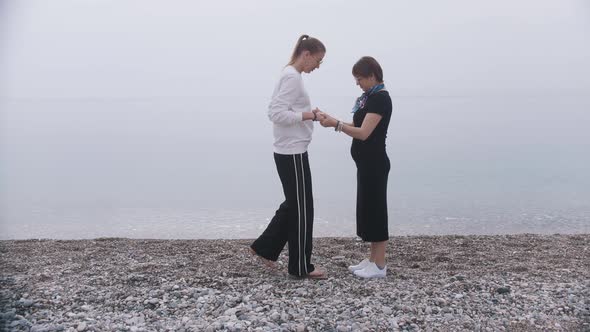 One Woman Holding Another By Her Hands and She Steps on the Sadhu Board on the Seashore alt