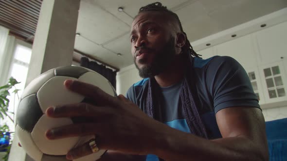 Portrait of Emotional Black Man with Soccer Ball Watching Football Game on Tv alt