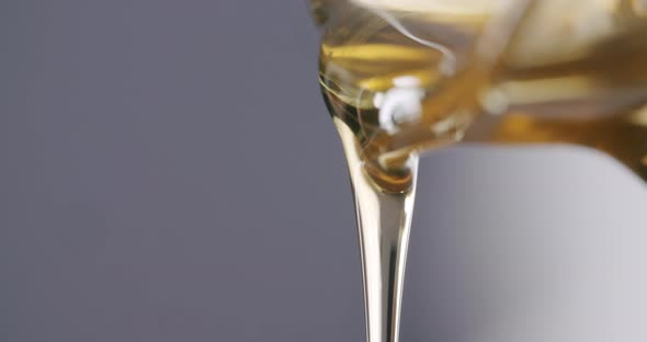 Macro close up shot of viscous honey flowing out of a honey jar before a grey studio background. Sta alt