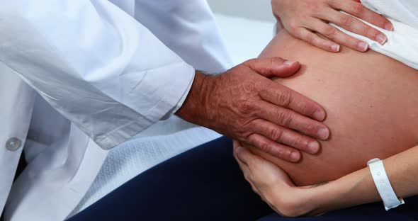 Mid section of doctor touching pregnant womans belly in ward alt