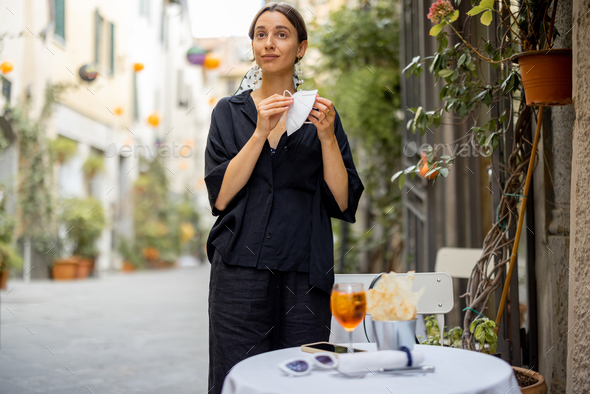 Woman takes off face mask while sitting at italian restaurant outdoors