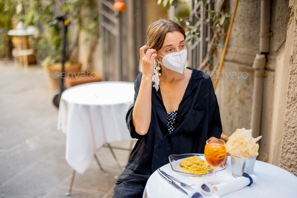 Woman takes off face mask while sitting at italian restaurant outdoors