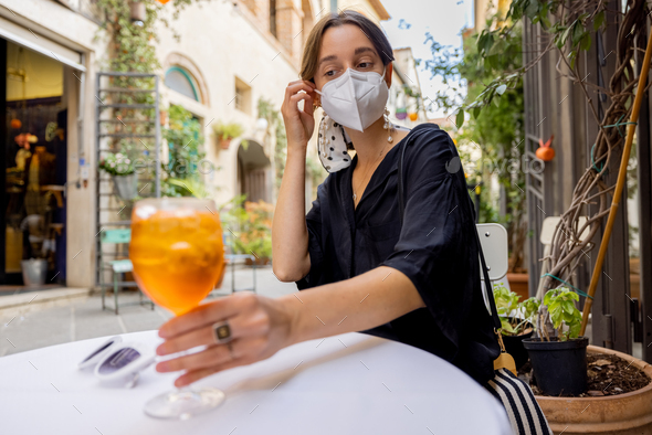 Woman takes off face mask while sitting and drinking wine at italian restaurant outdoors