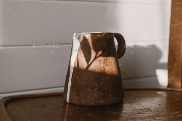 Home aesthetics. Modern ceramic kettle in sunlight on rustic wooden chair and leaves shadow