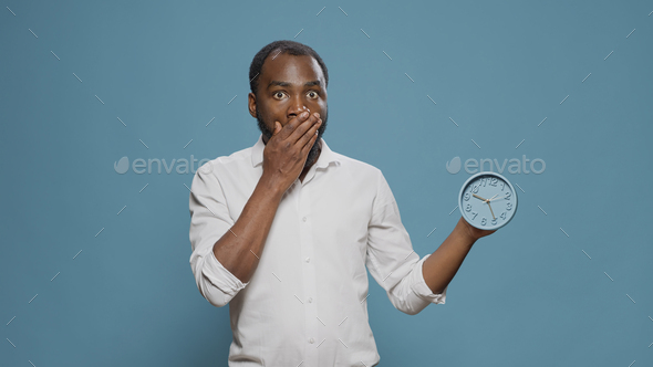 Shocked man checking time on clock and running late to work