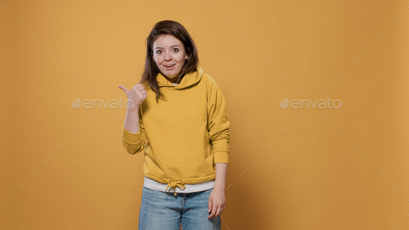 Funny smiling expressive woman doing mocking gesture with thumbs up pointing to the left and right