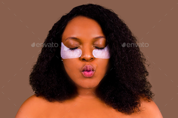 Attractive woman applying anti-fatigue under-eye mask in studio brown background
