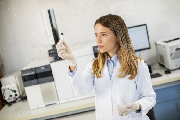 Young female scientist in a white lab coat preparing vial with a sample - Stock Photo - Images