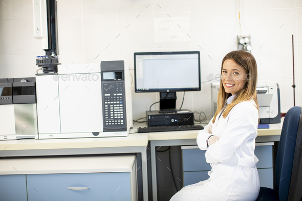 Female scientist in white lab coat sitting by the gas chromatography equipment in the biomedical lab
