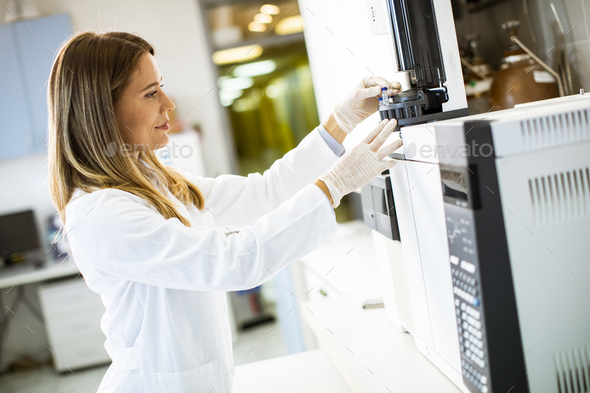 Young female scientist in a white lab coat putting vial - Stock Photo - Images