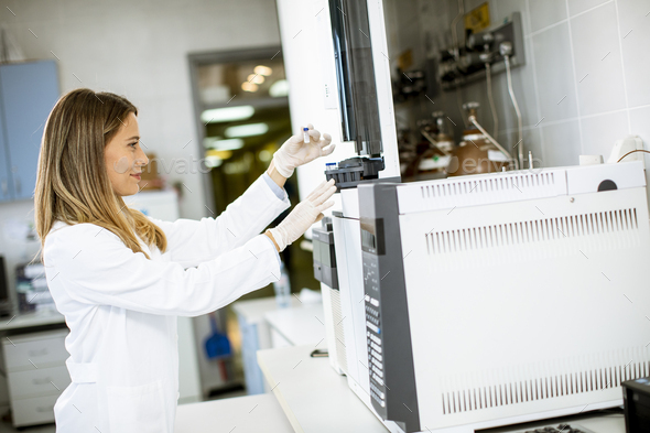 Young female scientist in a white lab coat putting vial - Stock Photo - Images