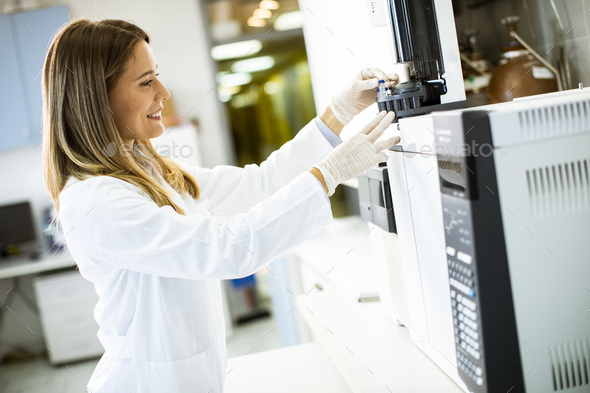 Young female scientist in a white lab coat putting vial - Stock Photo - Images