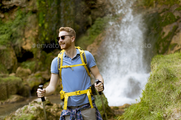 Young hiker stopped beside a mountain waterfall to rest