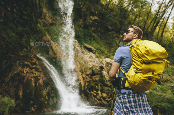 Young hiker stopped beside a mountain waterfall to rest
