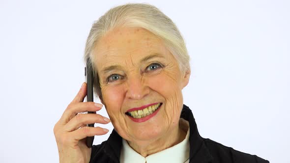 An Elderly Woman Talks on A Smartphone and Looks at The Camera alt