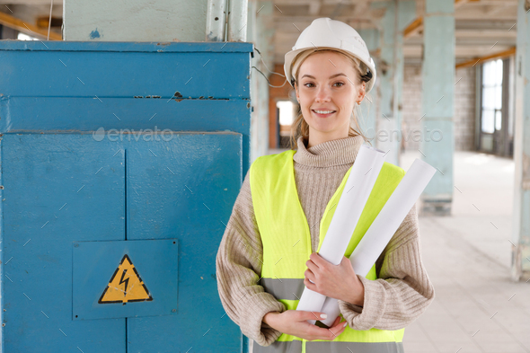 Young female maintenance engineer with blueprints at old electrical shield