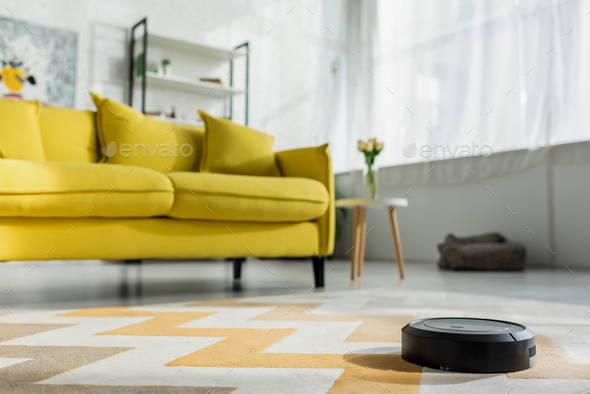 selective focus of robotic vacuum cleaner washing carpet near sofa in living room