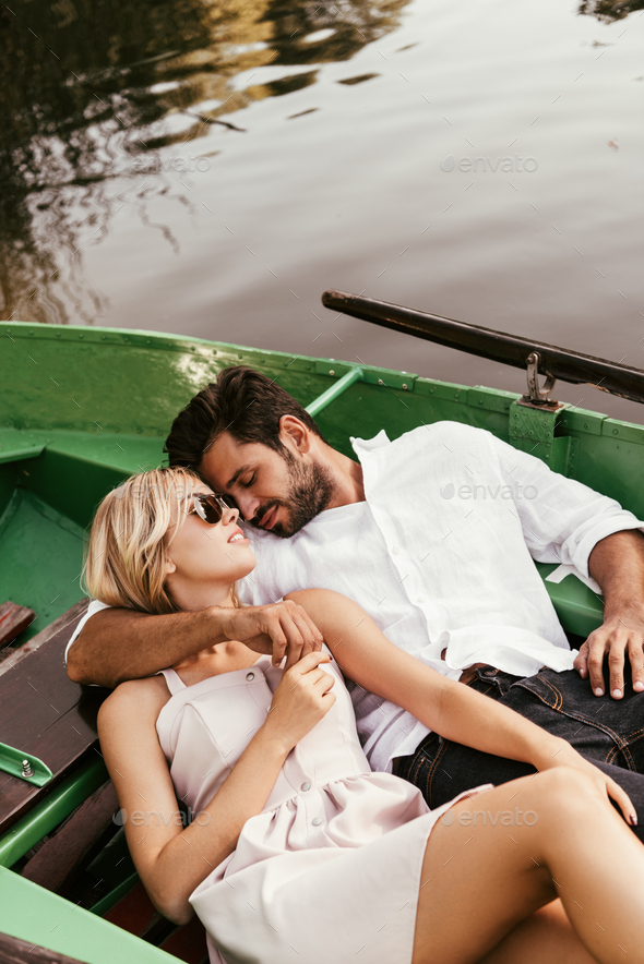 happy young couple embracing while relaxing in boat on lake
