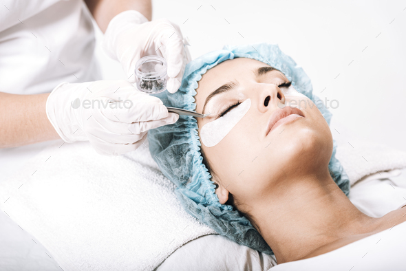 eyelash master putting false eyelashes with tweezers on model face isolated on white