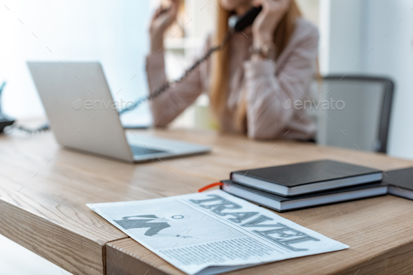 selective focus of travel newspaper and notebooks on desk near travel agent talking on phone