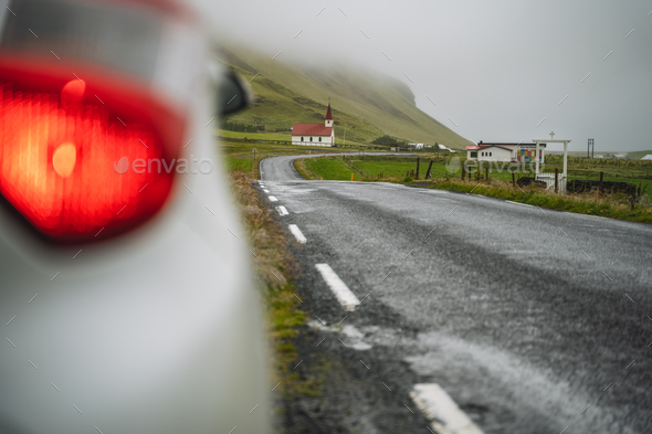 Car stoped on the road with view of typical rural Icelandic Church with red roof in Vik region