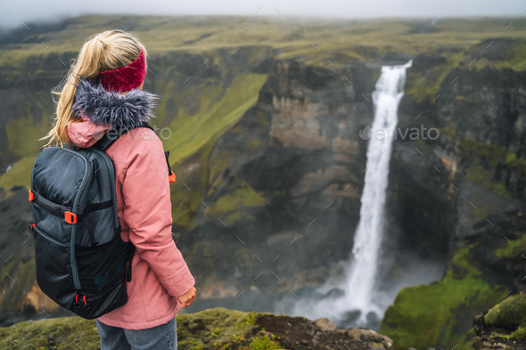 Woman with backpack and lilac jacket enjoying Haifoss waterfall of Iceland Highlands in