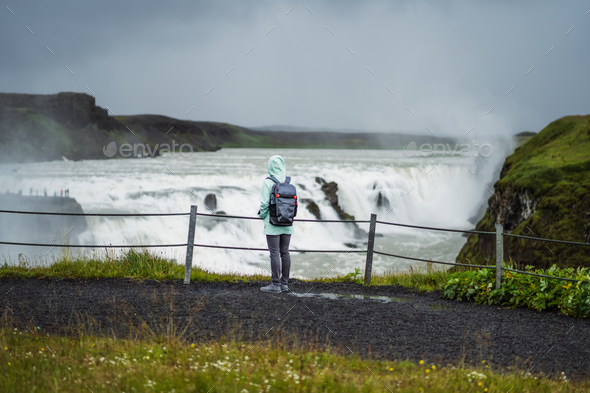 Woman with backpack and green jacket visit Gullfoss powerful famous waterfall in Iceland. Tourist - Stock Photo - Images