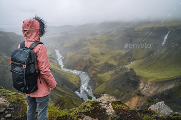 Woman wearing lilac jacket with backpack enjoying icelandic highland and river fossa close to - Stock Photo - Images