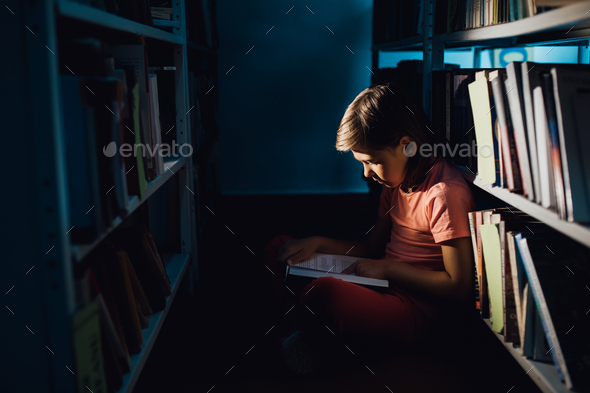 little girl reading a book in the library, sitting down, profile view, indoors,