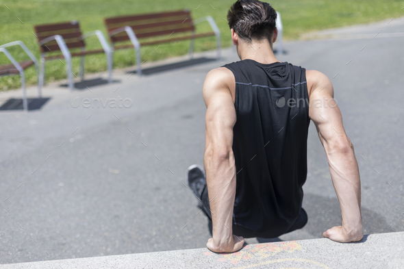 Young fit man doing triceps dips exercises during outdoor cross training workout